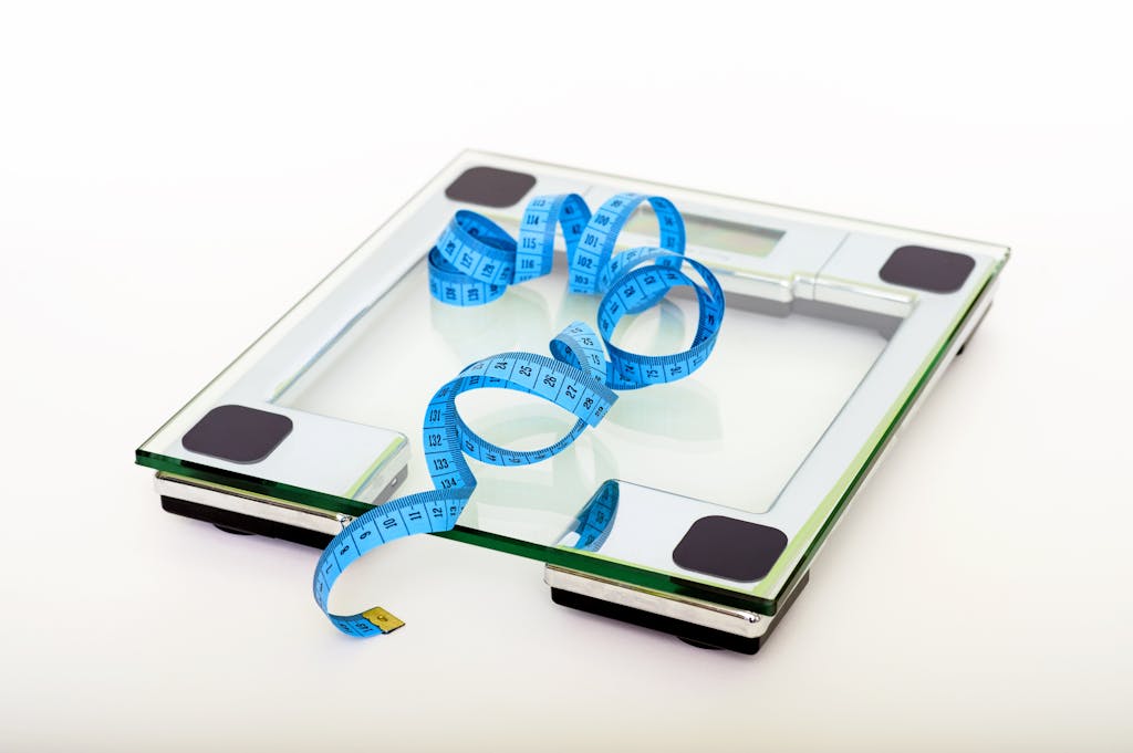 A digital glass weighing scale with a blue measuring tape, symbolizing weight management from a weight loss dietitian. 