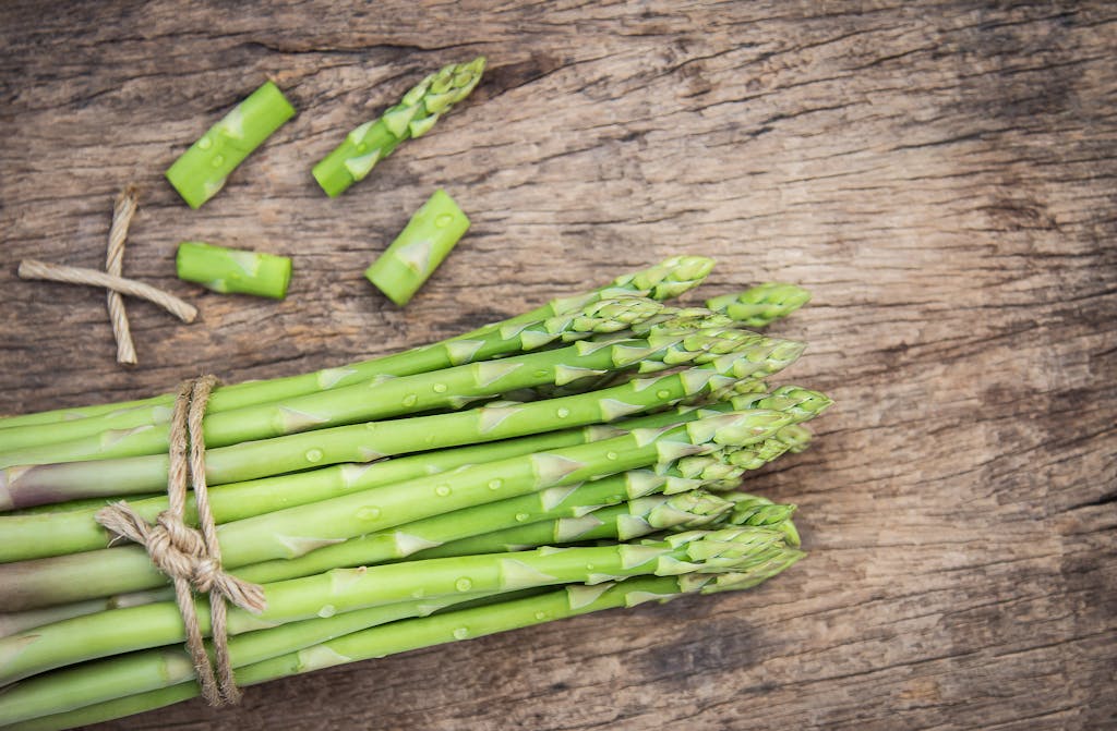 Bundle of fresh organic asparagus on a rustic wooden table, showcasing vibrant green colors and natural texture.