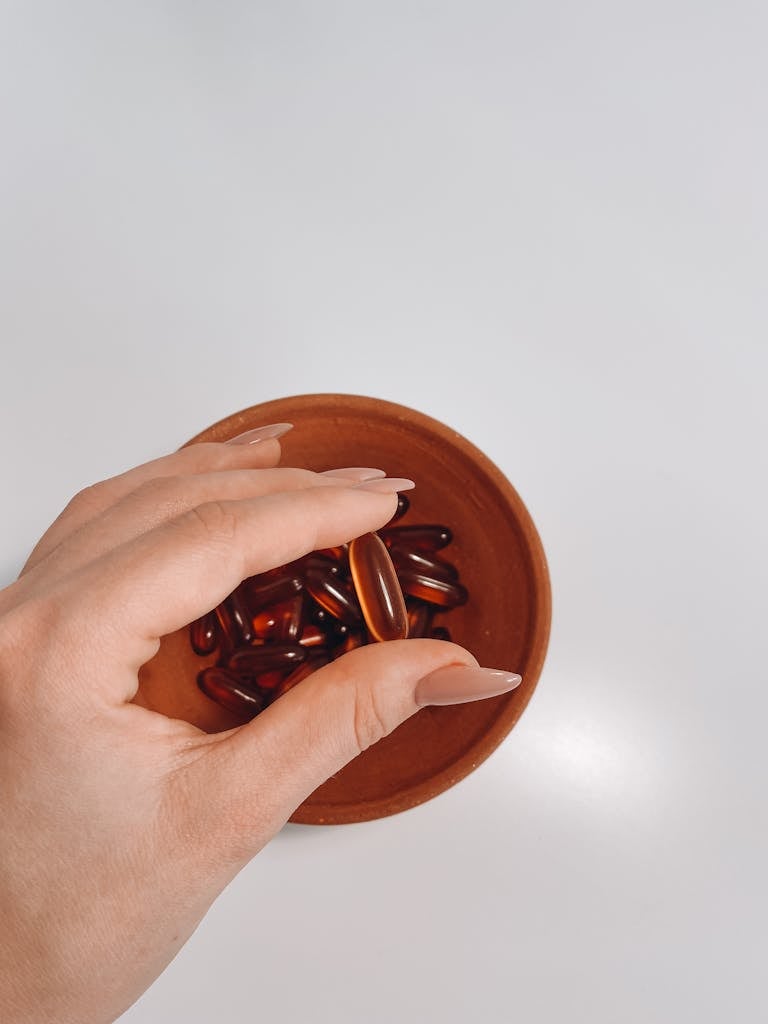 Close-up shot of a hand holding vitamin pills out of a terracotta bowl on a white background.